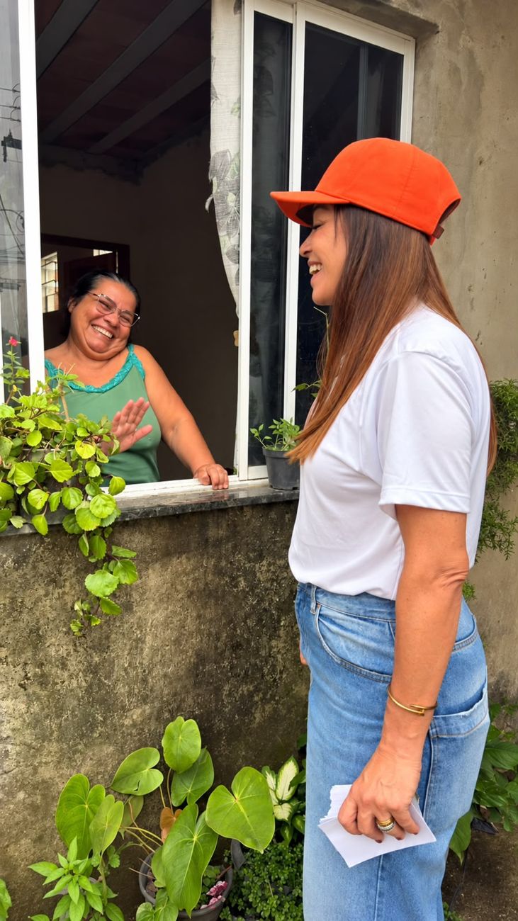 Kelaine conversa e ri com uma moradora na janela de casa